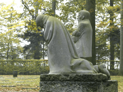 Stenen beeld van treurend ouderpaar op kerkhof tussen de bomen